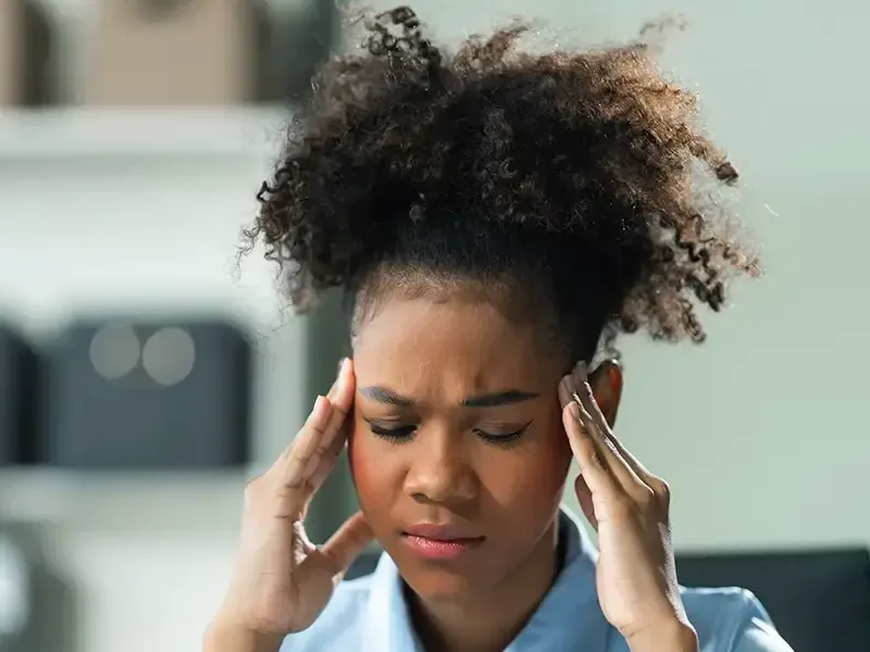 A young woman with her fingertips at both temples, eyes closed against the pressure in her head