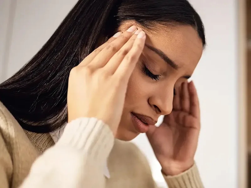 A woman with her fingers at her temples and her eyes closed as the room moves around her