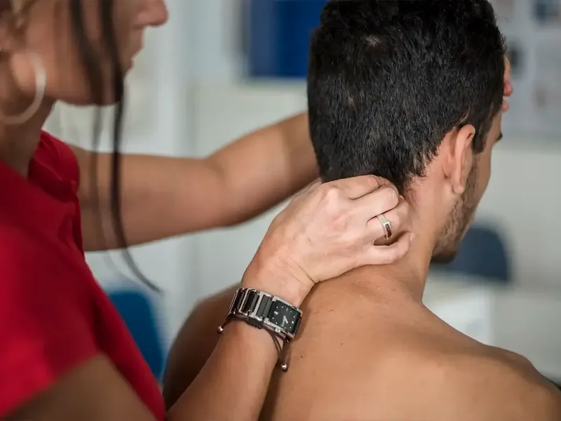A clinician assessing the neck and upper back of a seated patient