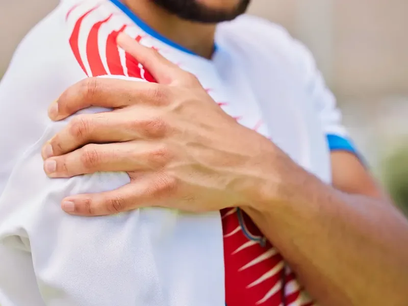 An athlete in a team jersey gripping his shoulder after a movement went wrong