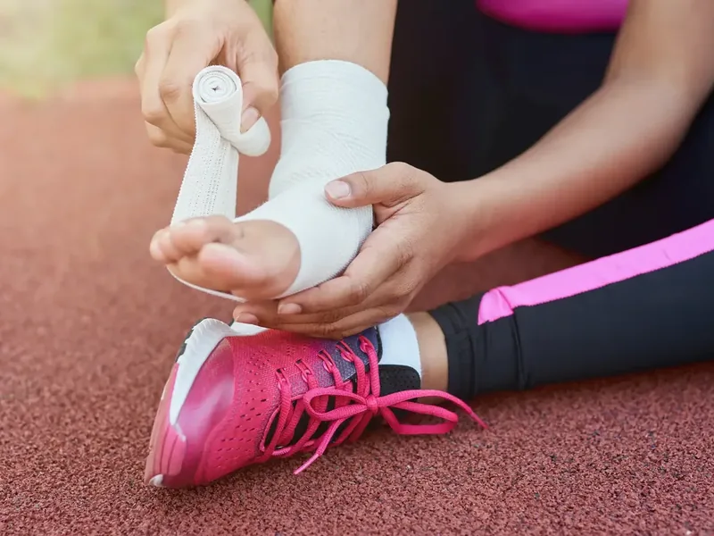 An ankle being wrapped at the side of a running track
