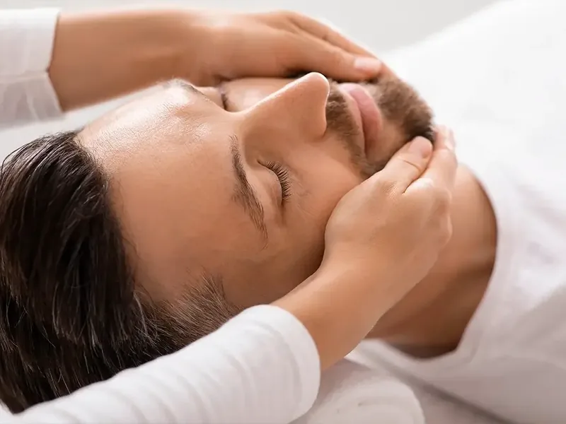 A clinician working along the jaw and temple of a patient lying down
