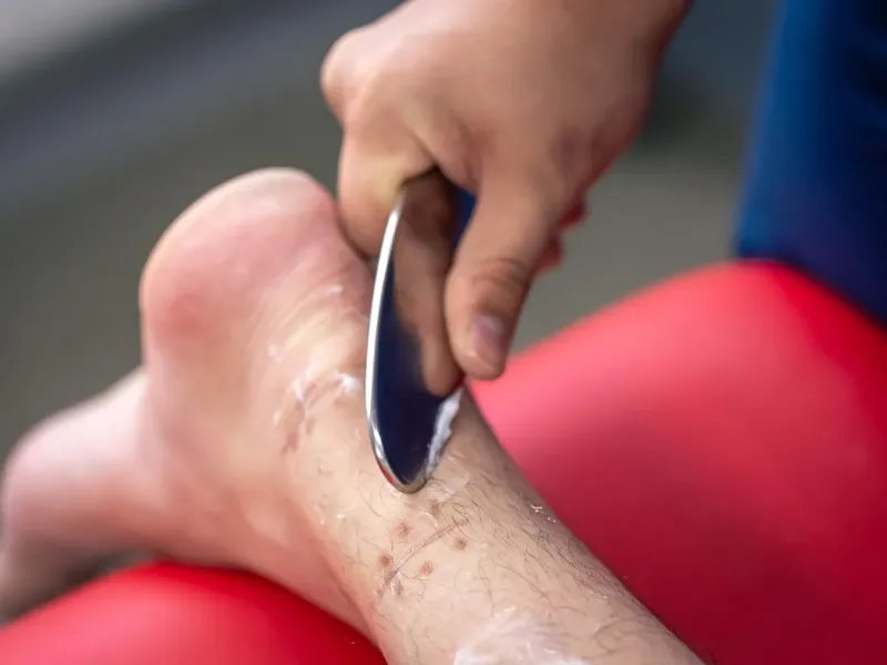 Doctor of Physical Therapy drawing a stainless steel IASTM tool along a patient's shoulder